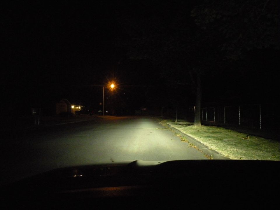 View from inside a car at night, headlights on a dark street with a single streetlight