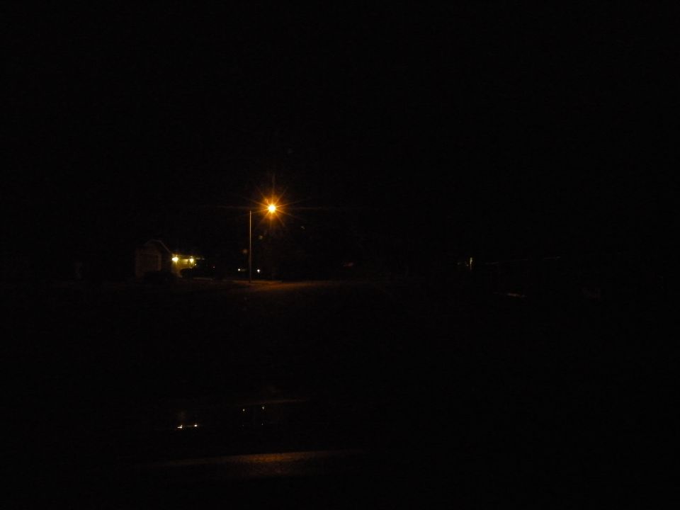 street lamp illuminates a dark road with a building in the distance