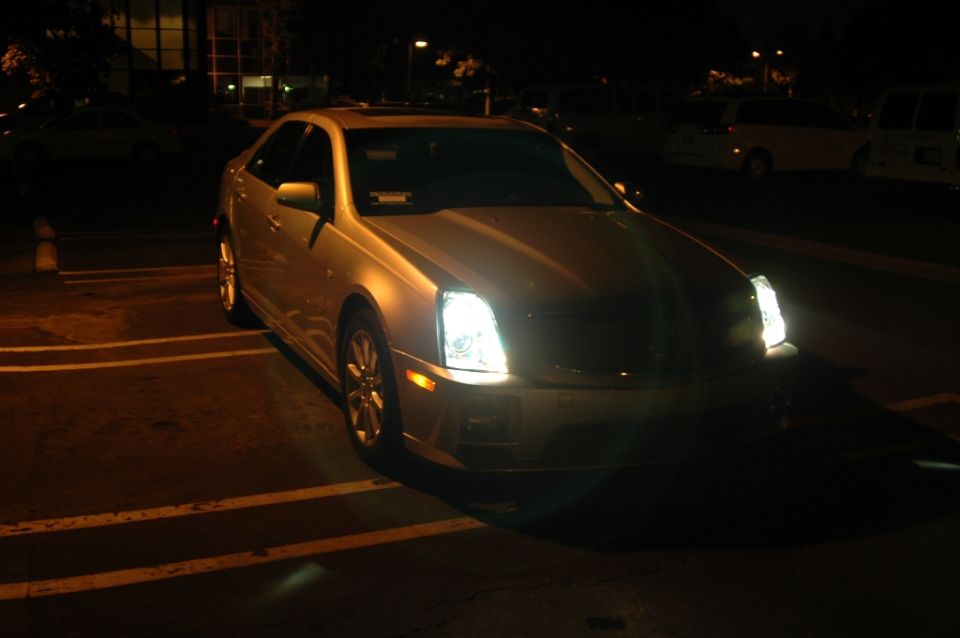 Silver Cadillac STS sedan at night in a parking lot with headlights on