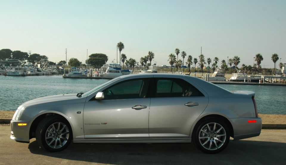 Silver Cadillac STS-V sedan side profile parked beside a boat harbor
