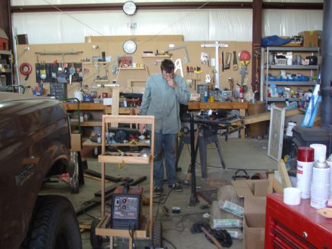 1993 Ford Bronco - A man works in a cluttered workshop next to a brown 1993 Ford Bronco.