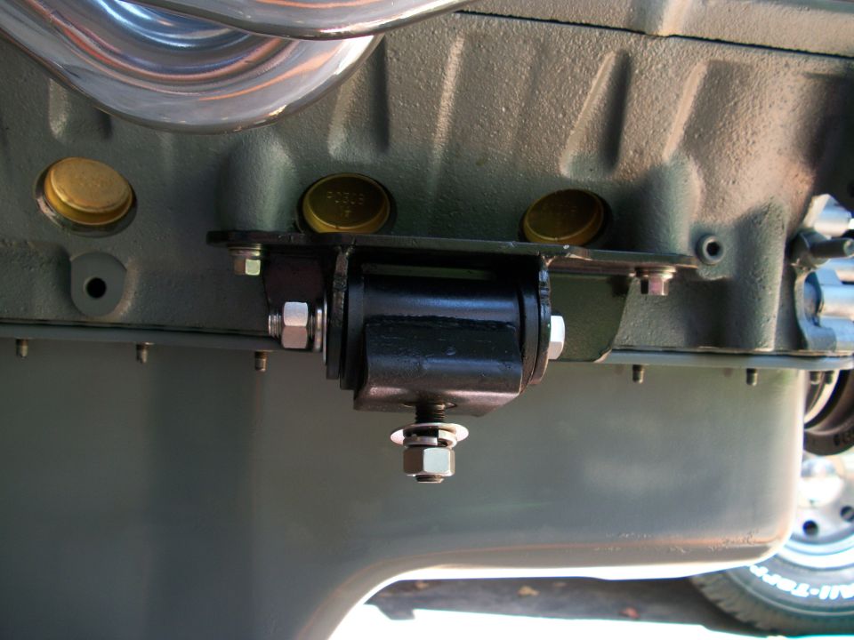Black engine mount bolted to gray-green engine block with brass freeze plugs and header