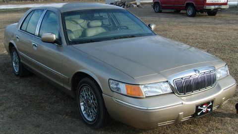 2000 Mercury Grand Marquis - This gold 2000 Mercury Grand Marquis sedan is parked on a dirt lot with a red truck in the background.