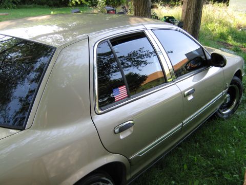 2000 Mercury Grand Marquis - A tan sedan is parked on grass with trees in the background. An American flag sticker is visible on the rear passenger window.