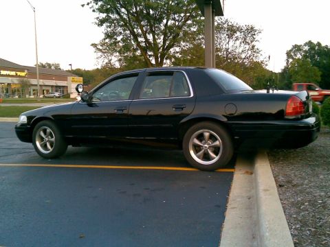 2003 Ford Crown Victoria - A black 2003 Ford Crown Victoria is parked in a lot, with its rear wheels on a concrete curb.
