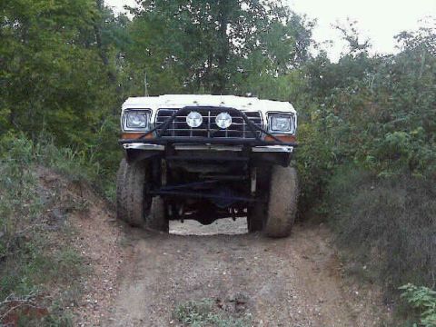 1979 Ford Bronco - This 1979 Ford Bronco is captured from the front, navigating an off-road trail with its distinctive bull bar and large tires.