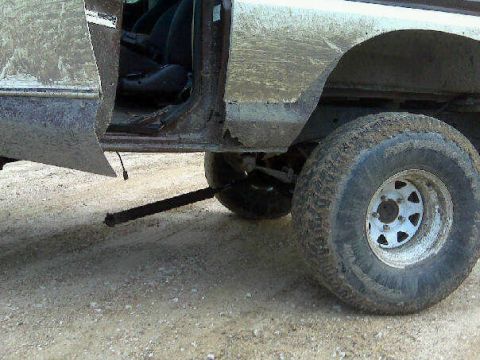1979 Ford Bronco - Mud-covered vehicle interior and wheel with a black bar extending from underneath.
