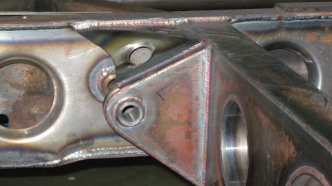 1995 Ford Bronco - Close-up of a custom-welded metal bracket with visible bolt holes and heat-affected metal.