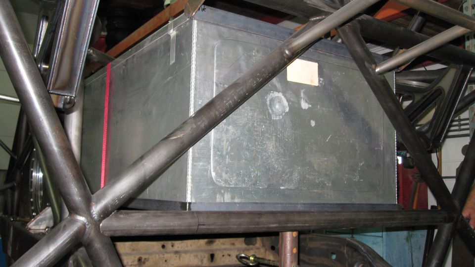 Custom metal fuel tank with red strap, surrounded by black roll cage tubing