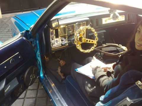 1991 Ford Crown Victoria - The interior of a blue car features a distinctive gold chain steering wheel and a woman seated inside.