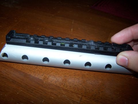 1986 Ford Bronco - A black gun scope mount rail is positioned over a white tube with multiple circular perforations.