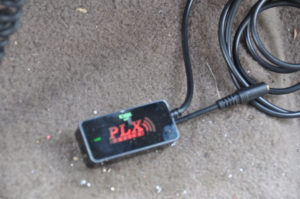 PLX device with red logo on car floor mat, connected to a black cable