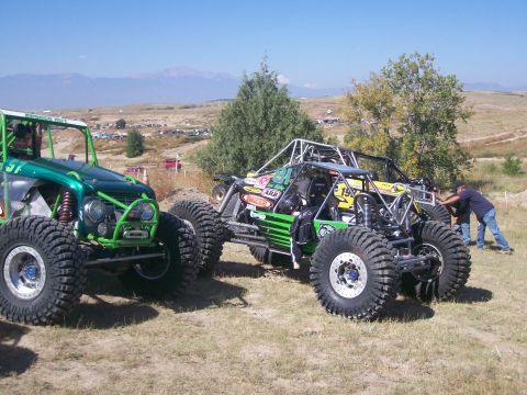 1993 Ford Bronco - Multiple custom off-road buggies are gathered on a grassy field under a clear blue sky.