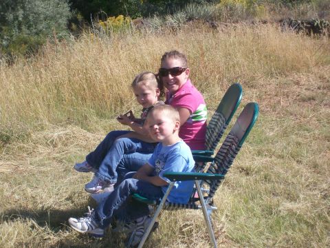 1993 Ford Bronco - A woman and two young children relax in folding chairs amidst dry grass and sparse vegetation under a sunny sky.