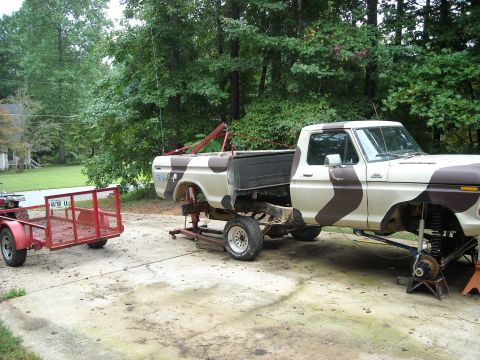 1979 Ford F-150 - A pickup truck is raised on jack stands for maintenance, with a small trailer parked to its left.