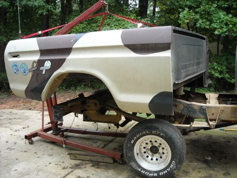 1979 Ford F-150 - The side of a truck bed, painted in camouflage, is suspended by a hoist. It has three circular stickers on the rear quarter panel.