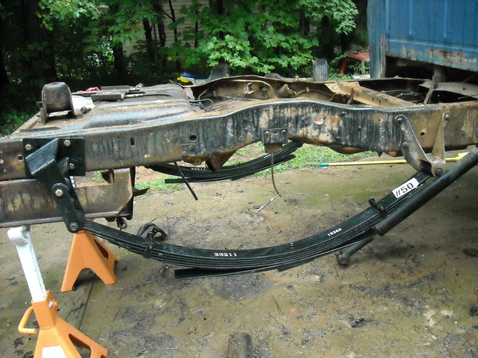 Truck frame on jack stands with leaf springs removed. Part numbers visible on springs