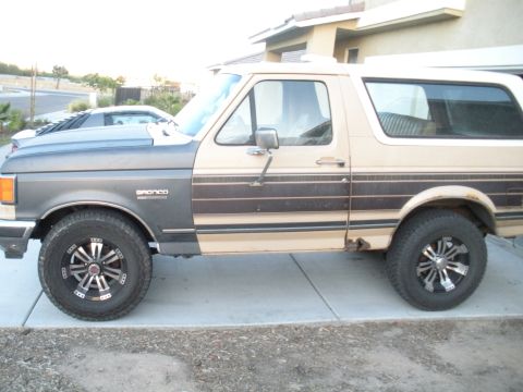 1990 Ford Bronco - Side view of a two-tone Ford Bronco, displaying its distinctive body style and some signs of wear.