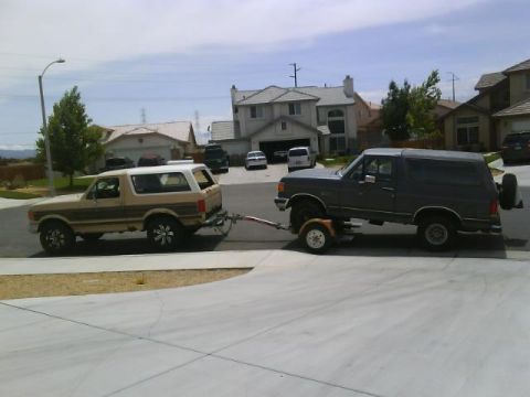 1990 Ford Bronco - Two Ford Broncos are seen side-by-side, with the rear vehicle being towed by the front one.