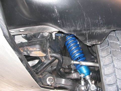 1990 Ford Bronco - blue coilover shock and suspension linkage mounted inside a vehicle's wheel well, viewed from below.