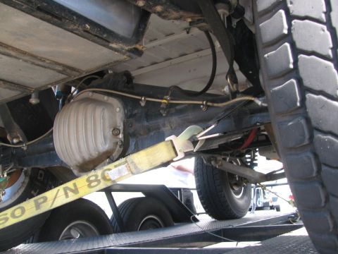 1990 Ford Bronco - Underbody view of a trailered vehicle showing the differential housing, rear axle and a yellow tie-down strap.