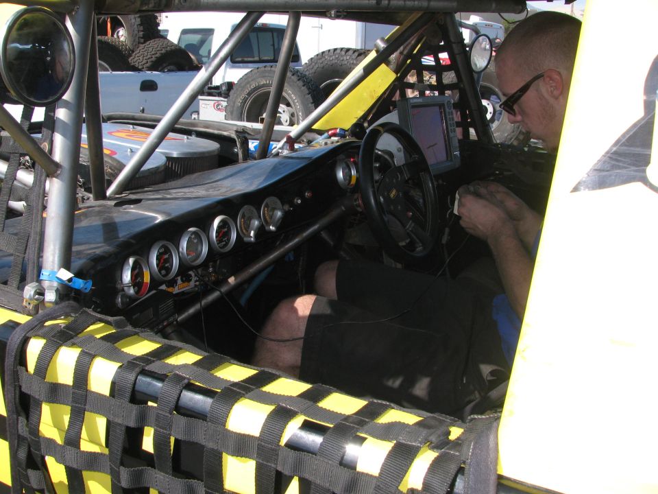 Man working inside a tube-chassis off-road racer cockpit with gauges and screen