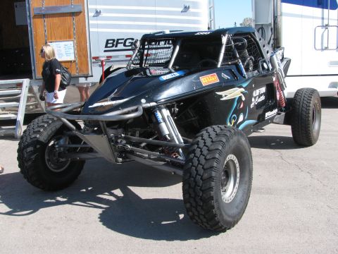 1990 Ford Bronco - black tube-chassis off-road race buggy with long-travel suspension parked beside transport trailers.