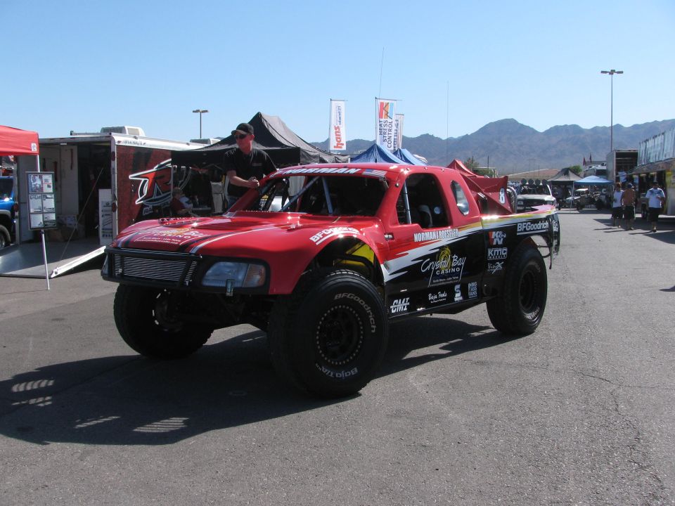 Red off-road race truck with sponsor decals and roof light in desert pit area