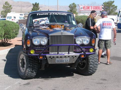 1990 Ford Bronco - purple Rolls-Royce sedan converted into an off-road racer with a brush guard, knobby tires, and a Welcome to Scoreville banner behind.