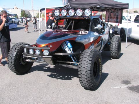 1990 Ford Bronco - gray and orange open tube-frame off-road race buggy numbered 199 with a roof light bar parked in a desert pit area.