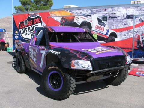 1990 Ford Bronco - purple off-road race truck numbered 7 with Super Clean graphics parked in front of a Lucas Oil Off Road Racing trailer.