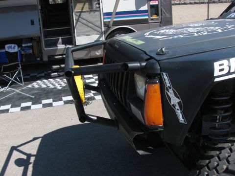 1990 Ford Bronco - close-up of a black off-road race vehicle's front corner showing the brush guard, headlight, amber marker, and coilover shock.