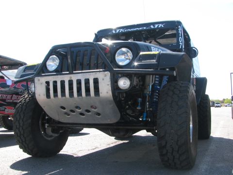 1990 Ford Bronco - Front view of a black Jeep-bodied off-road race vehicle with a tubular front bumper, dual round headlights, ATK Engines decals, and large m…