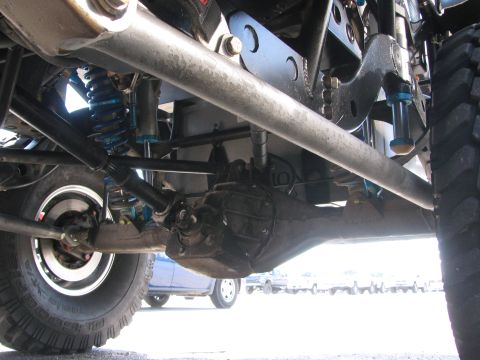 1990 Ford Bronco - Underbody view of an off-road race vehicle showing the rear differential, driveshaft, blue coilover shocks and beadlock wheels with mud tir…