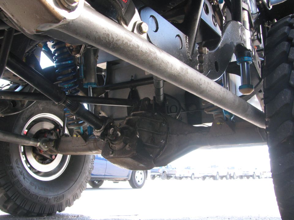 Undercarriage of an off-road race truck showing rear axle, blue coilover shocks and tires