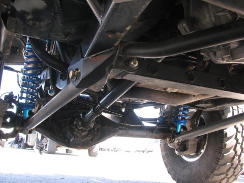 1990 Ford Bronco - Low-angle undercarriage shot of an off-road race rig showing blue coilover shocks, tubular control arms and skid plating.