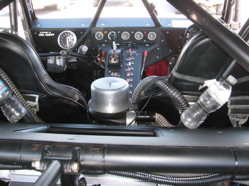 Rear-facing interior of a tube-chassis race car with seats, gauges and water bottles