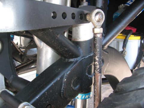 1990 Ford Bronco - Detail of an off-road race rig's suspension showing a black tubular link, a heim joint rod end, a steering shaft and shock components.