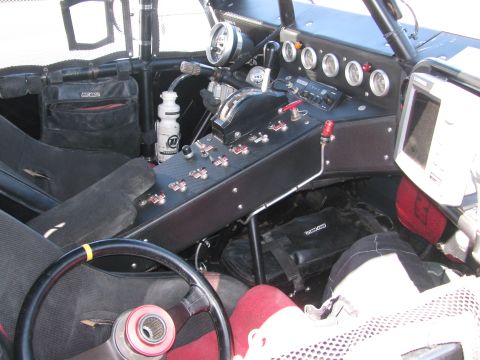 1990 Ford Bronco - Cockpit of an off-road race vehicle showing the steering wheel, a long switch-panel console, round gauges and racing seats.