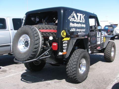 1990 Ford Bronco - Rear three-quarter view of a black off-road race Jeep with a tailgate-mounted spare tire and ATK Engines, Jeepspeed and AEM sponsor decals.