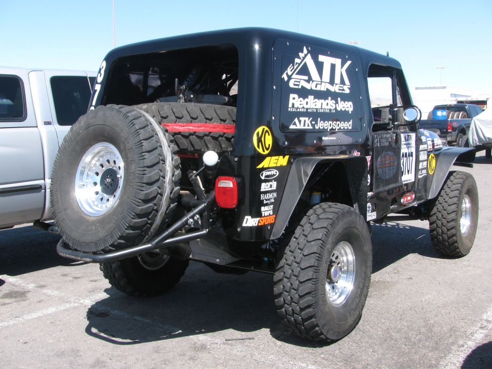 Rear three-quarter view of black ATK Jeepspeed race Jeep with spare tire and sponsor decals