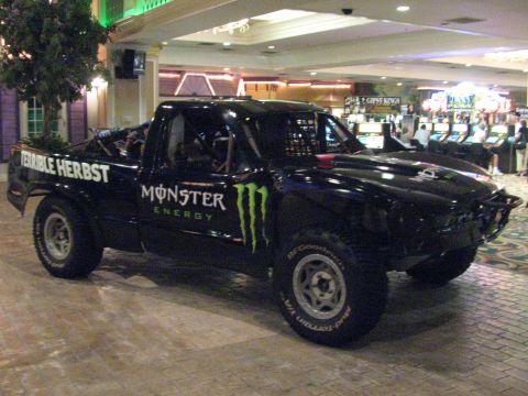 1990 Ford Bronco - black off-road trophy truck with Terrible Herbst and Monster Energy graphics on display indoors near slot or arcade machines.
