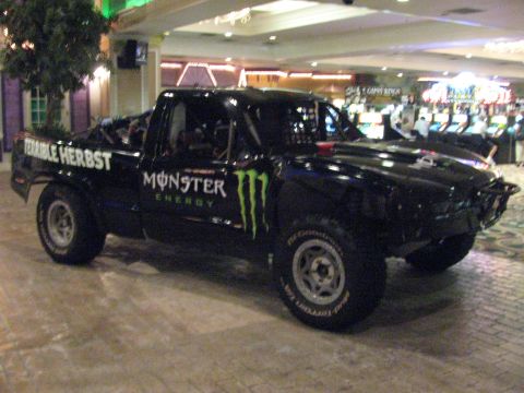 1990 Ford Bronco - Front three-quarter view of a black Terrible Herbst Monster Energy off-road trophy truck displayed on a tiled indoor floor.
