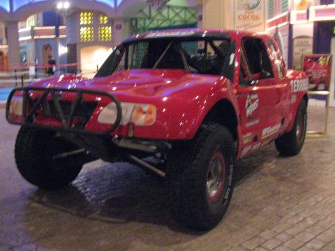 1990 Ford Bronco - Front view of a glossy red Terrible Herbst off-road trophy truck with a tubular front bumper on display indoors.