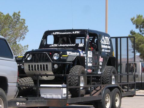 1990 Ford Bronco - black ATK Engines Jeepspeed number 302 off-road race Jeep sits on an open utility trailer under a blue sky.