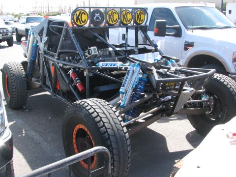 1990 Ford Bronco - bare tube-chassis off-road buggy with a roof-mounted KC light bar, blue coilover shocks and an exposed frame parked in a paddock.