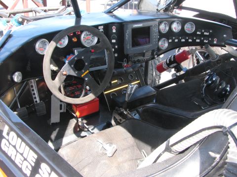 1990 Ford Bronco - Cockpit of an off-road race buggy showing the steering wheel, round gauges, a Lowrance GPS screen, fire extinguisher and bucket seat.