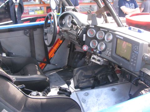 1990 Ford Bronco - Interior of an off-road race truck showing the steering wheel, cluster of round gauges, a Lowrance GPS screen and a bucket seat.