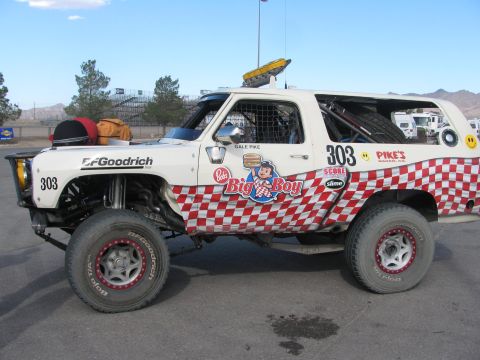 1990 Ford Bronco - Full side profile of the white number 303 desert race truck showing red checkered Big Boy graphics and large knobby tires.