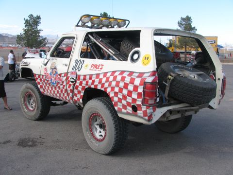 1990 Ford Bronco - Rear quarter of the white 303 race truck shows its checkered tailgate panel, roll cage and rear-mounted spare tires.